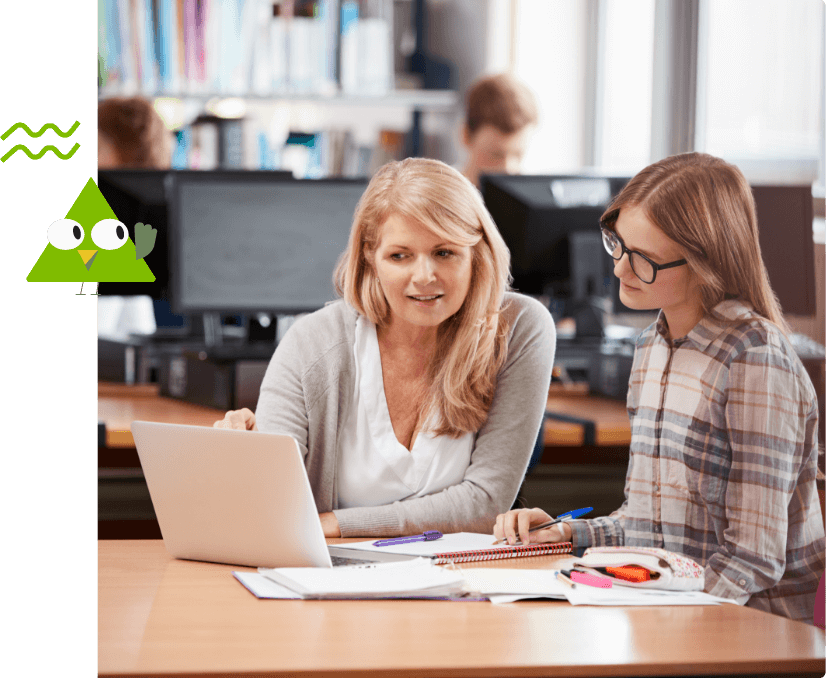 Tutor giving instruction to a student while pointing at the laptop on the table in front of them.